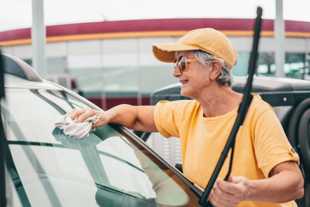 A Woman In A Cap Rinsing Down A Car's Windscreen